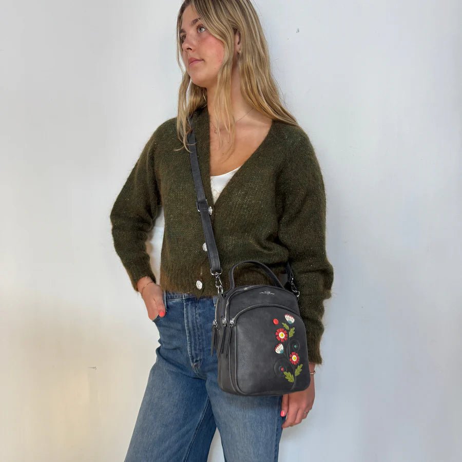 Woman holding a black handbag with floral embroidery against a white wall - okotoks hc pharmacy