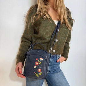 Person wearing a green sweater and blue jeans holding a dark blue handbag with floral embroidery. - okotoks hc pharmacy