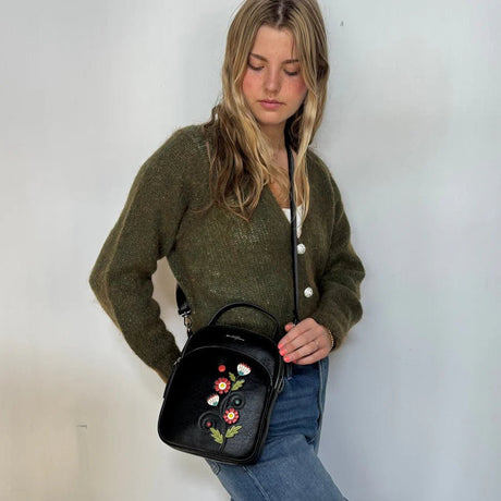 Woman holding a black handbag with floral embroidery against a white background - okotoks hc pharmacy