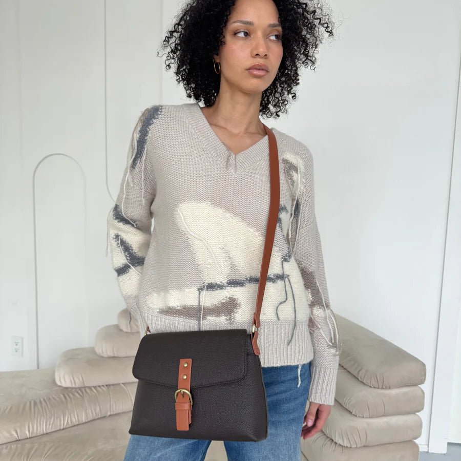Woman holding a brown handbag with a brown strap in a minimal indoor setting - okotoks hc pharmacy