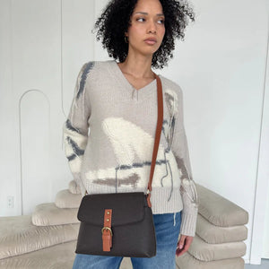 Woman holding a brown handbag with a brown strap in a minimal indoor setting - okotoks hc pharmacy
