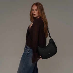 Woman holding a black handbag against a plain background - okotoks hc pharmacy