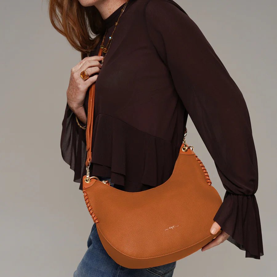 Person holding a brown leather handbag against a neutral background - okotoks hc pharmacy