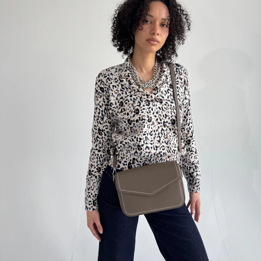 Woman wearing a leopard print top and holding a grey handbag against a white background- okotoks hc pharmacy