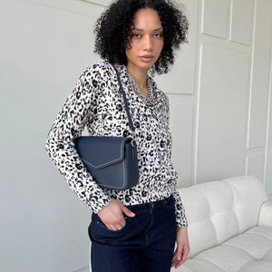 Woman wearing a leopard print shirt and holding a blue handbag in a room with a white couch. - okotoks hc pharmacy