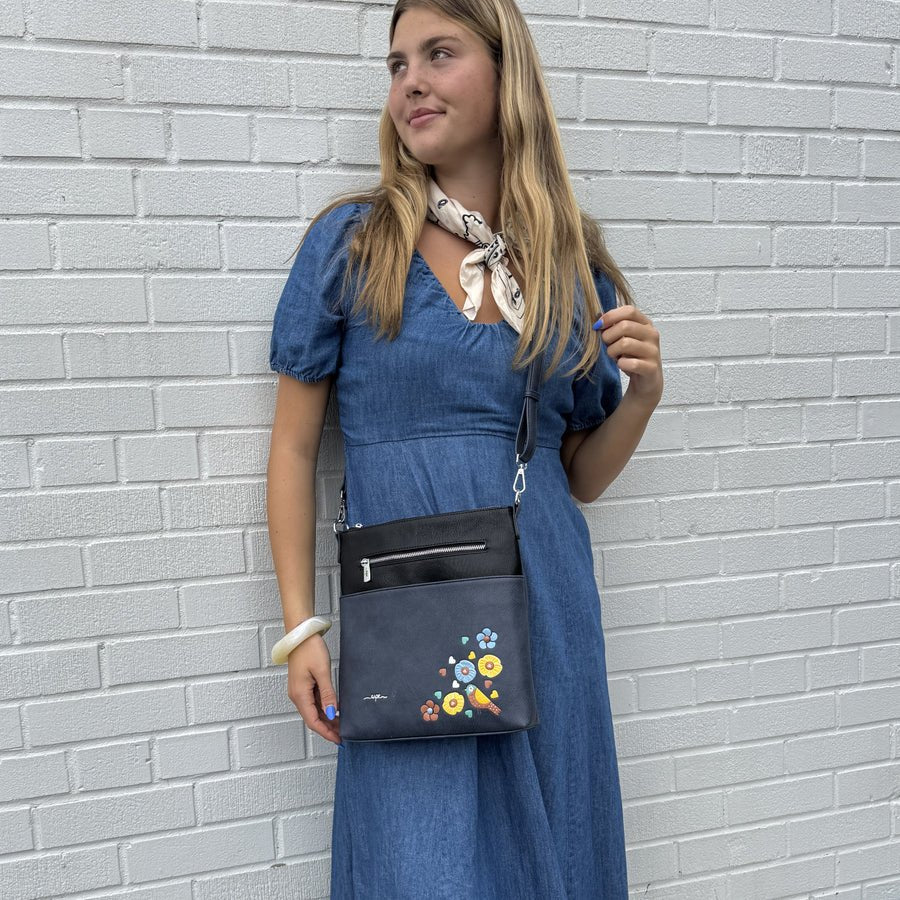 Woman in a blue dress holding a black handbag with floral designs against a gray brick wall. - okotoks hc pharmacy