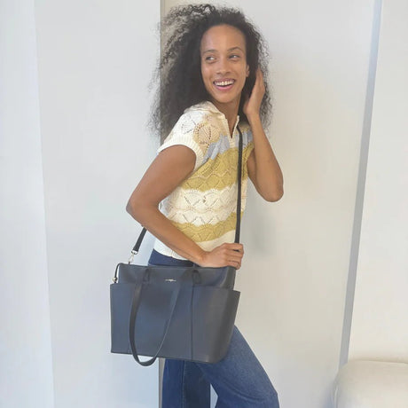 Woman holding a black handbag against a plain background - okotoks hc pharmacy