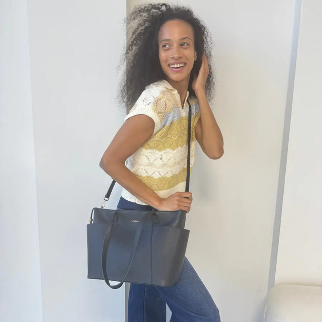 Woman holding a black handbag against a plain background - okotoks hc pharmacy