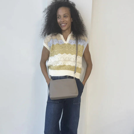 Woman wearing a patterned sleeveless top and jeans, holding a beige crossbody bag against a plain background. - okotoks hc pharmacy