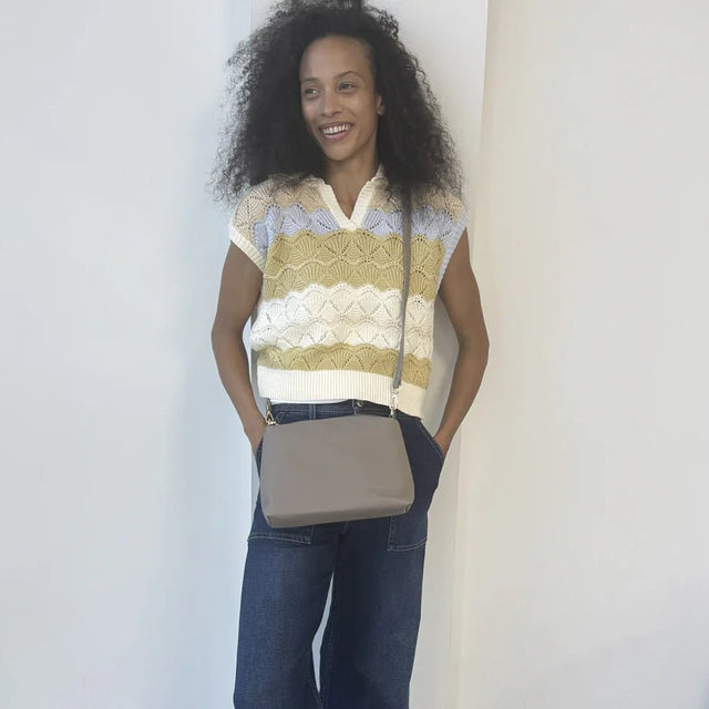 Woman wearing a patterned sleeveless top and jeans, holding a beige crossbody bag against a plain background. - okotoks hc pharmacy