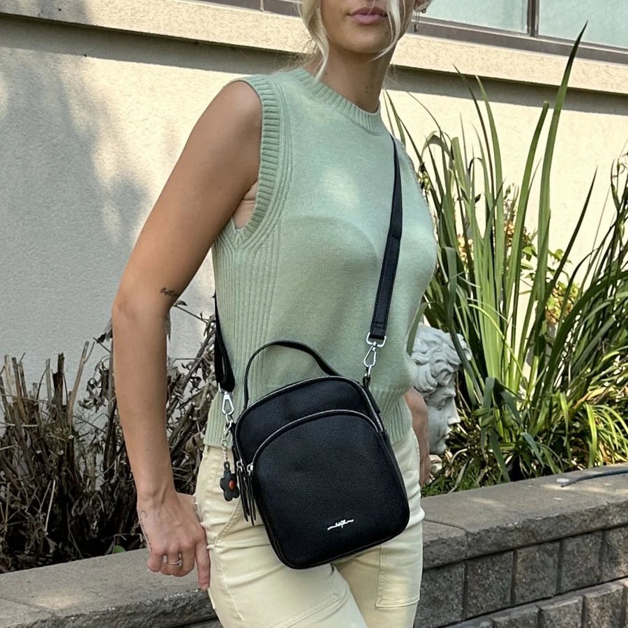 Woman holding a black handbag outdoors with plants and a wall in the background - okotoks hc pharmacy