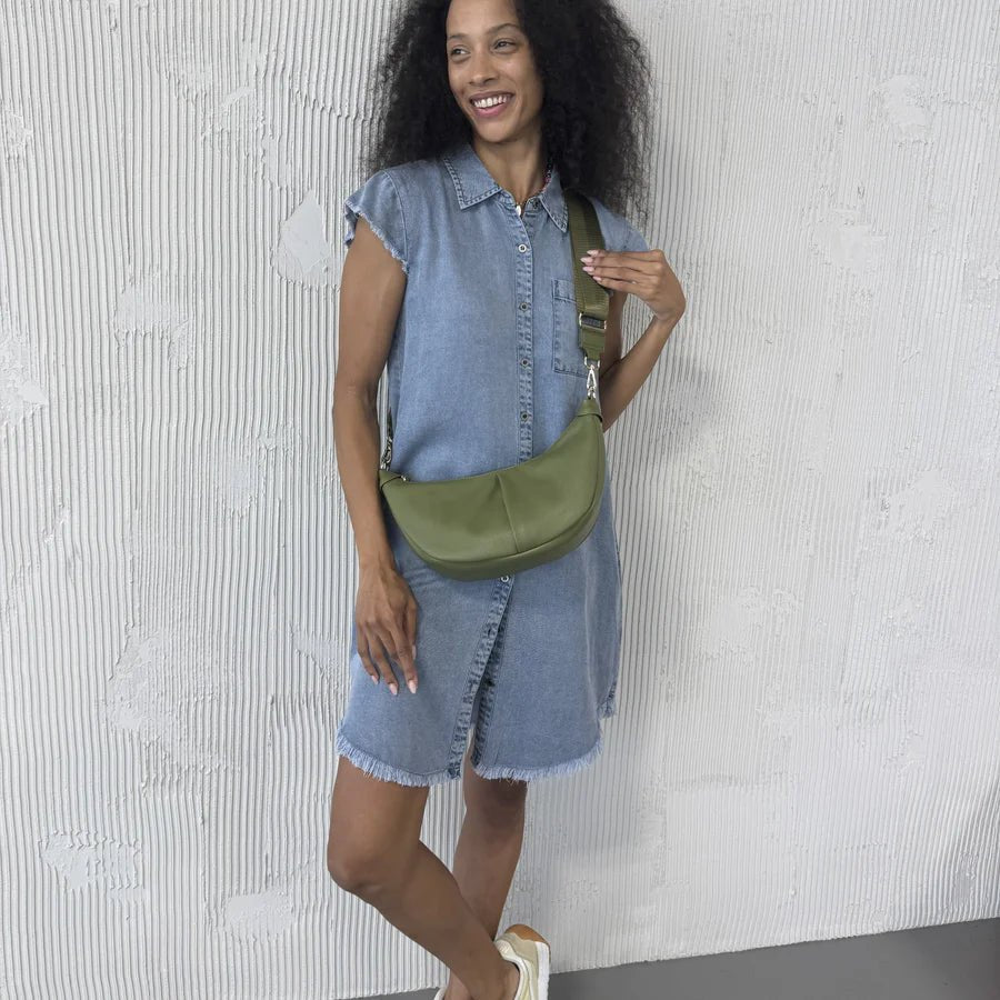 Woman wearing a denim dress with a green crossbody bag against a textured white wall. - okotoks hc pharmacy