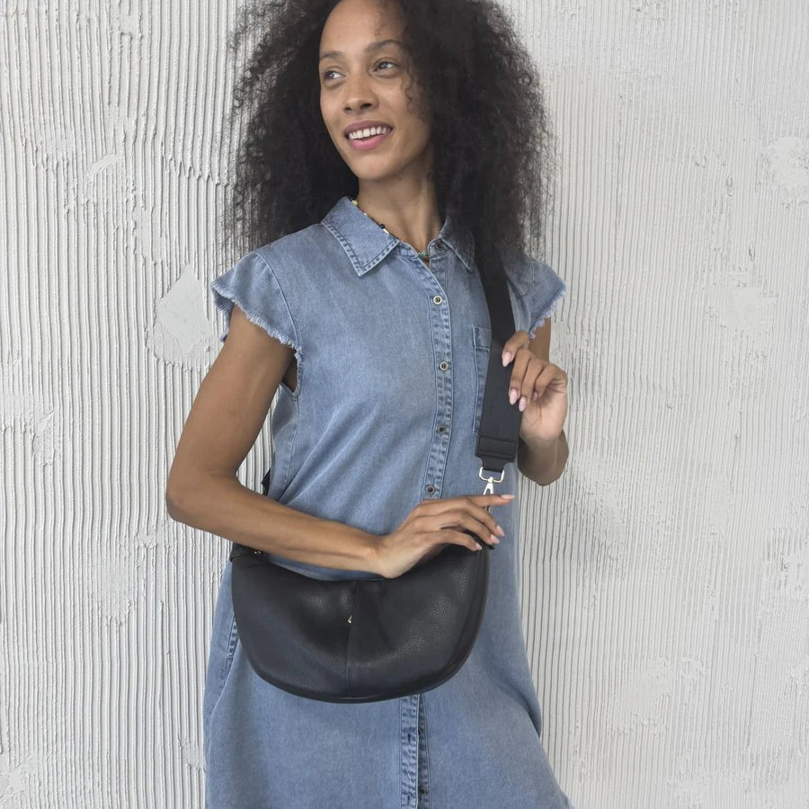 Woman holding a black leather bag against a textured white wall - okotoks hc pharmacy