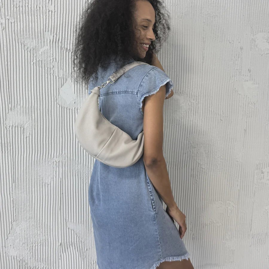 Woman wearing a denim dress with a beige bag against a textured white wall - okotoks hc pharmacy