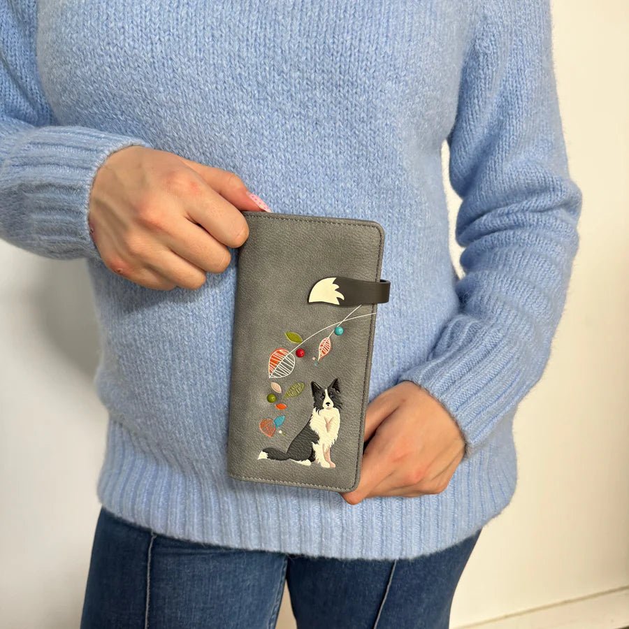 Person holding a gray wallet with a dog design, wearing a blue sweater. - okotoks hc pharmacy