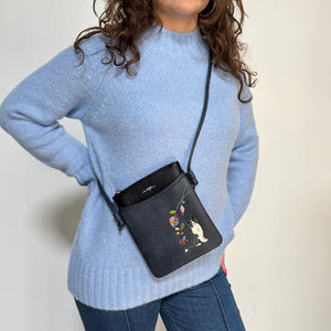 Person wearing a blue sweater with a black crossbody bag featuring floral designs. - okotoks hc pharmacy