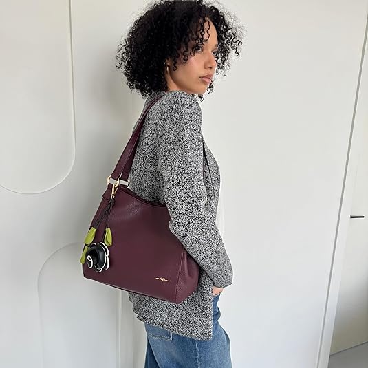 Woman carrying a plum handbag with a visible brand logo against a white background - okotoks hc pharmacy