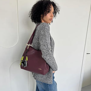 Woman carrying a plum handbag with a visible brand logo against a white background - okotoks hc pharmacy