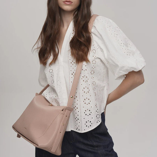 Woman holding a beige handbag wearing a white blouse with a subtle pattern. - okotoks hc pharmacy