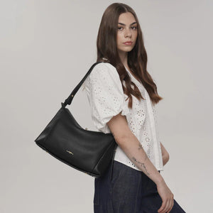 Woman holding a black handbag against a plain background - okotoks hc pharmacy