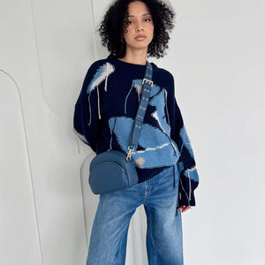Woman wearing a blue and navy patterned sweater with wide-leg jeans, holding a matching blue handbag. - okotoks hc pharmacy