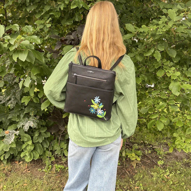 Person wearing a black backpack with floral embroidery in a green outdoor setting - okotoks hc pharmacy