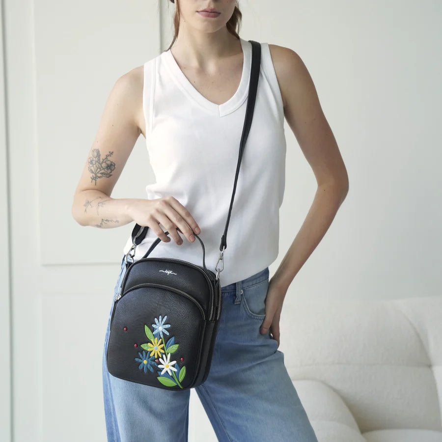 Person holding a black crossbody bag with floral embroidery against a white background - okotoks hc pharmacy