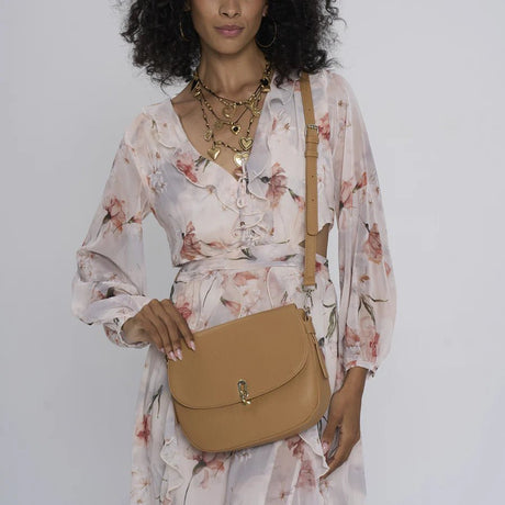 Woman holding a tan handbag against a plain background - okotoks hc pharmacy