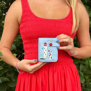 Person wearing a red dress holding a blue cardholder with a lighthouse design against a green leafy background - okotoks hc pharmacy