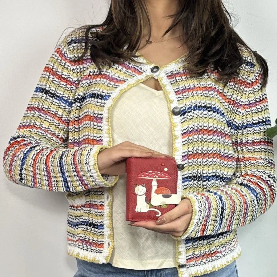 Person wearing a colorful striped jacket holding a red wallet with a cat design. - okotoks hc pharmacy