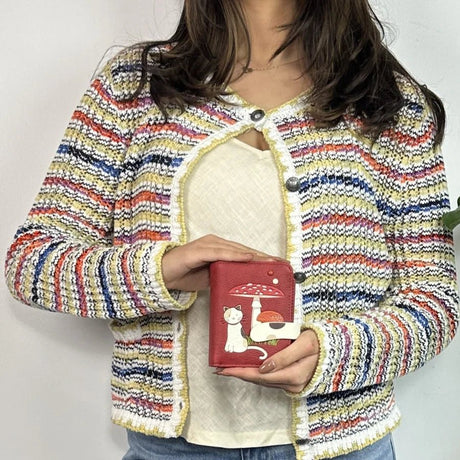 Person wearing a colorful striped jacket holding a red wallet with a cat design. - okotoks hc pharmacy