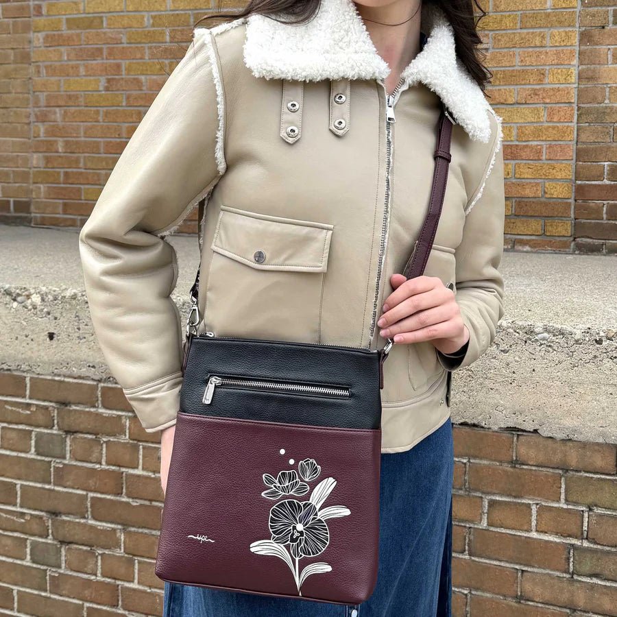 Person holding a wine crossbody bag with floral design against a brick wall. - okotoks hc pharmacy