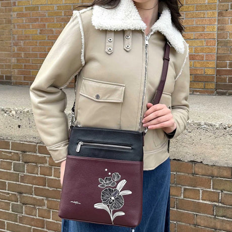 Person holding a wine crossbody bag with floral design against a brick wall. - okotoks hc pharmacy