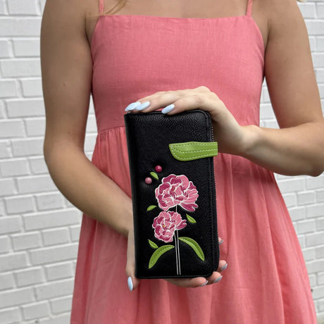 Person holding a black wallet with floral embroidery against a white brick wall. - okotoks hc pharmacy