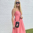 Woman in a pink dress holding a black crossbody bag with floral design against a white brick wall. - okotoks hc pharmacy