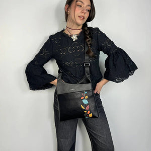 Woman holding a black bag with colorful floral embroidery against a white background - okotoks hc pharmacy