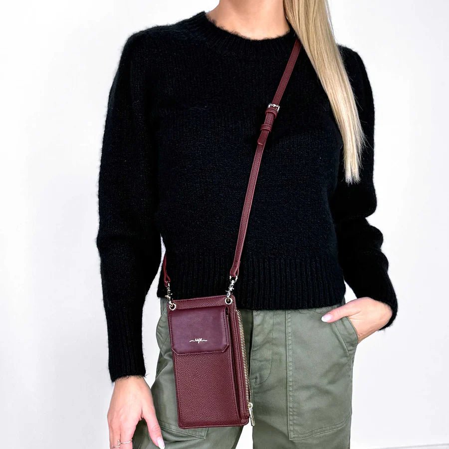 Person wearing a black sweater and green pants with a burgundy crossbody bag on a white background - okotoks hc pharmacy