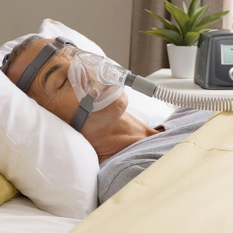 Person using a CPAP machine in bed with a plant in the background - okotoks hc pharmacy