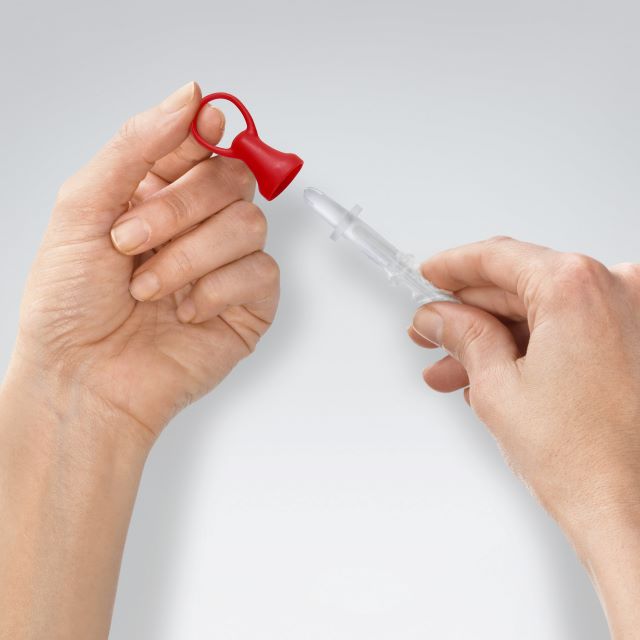 Person holding a clear tip with a red cap against a light gray background - okotoks hc pharmacy