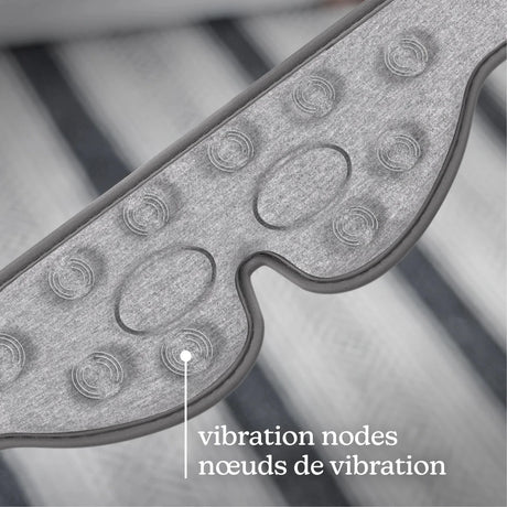 Close-up of a gray textured wearable device with oval and circular vibration nodes, overlaid with the text 'vibration nodes / nœuds de vibration' on a blurred striped background. - okotoks hc pharmacy