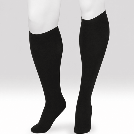 A pair of black knee-high compression socks or calf sleeves shown on a white mannequin lower leg and foot form against a light gray studio background. - okotoks hc pharmacy