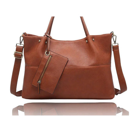 A brown pebbled leather tote bag with dual top handles, a detachable shoulder strap, and a matching zippered pouch hanging from a gold-tone zipper, shown on a white background with a reflection below. - okotoks hc pharmacy