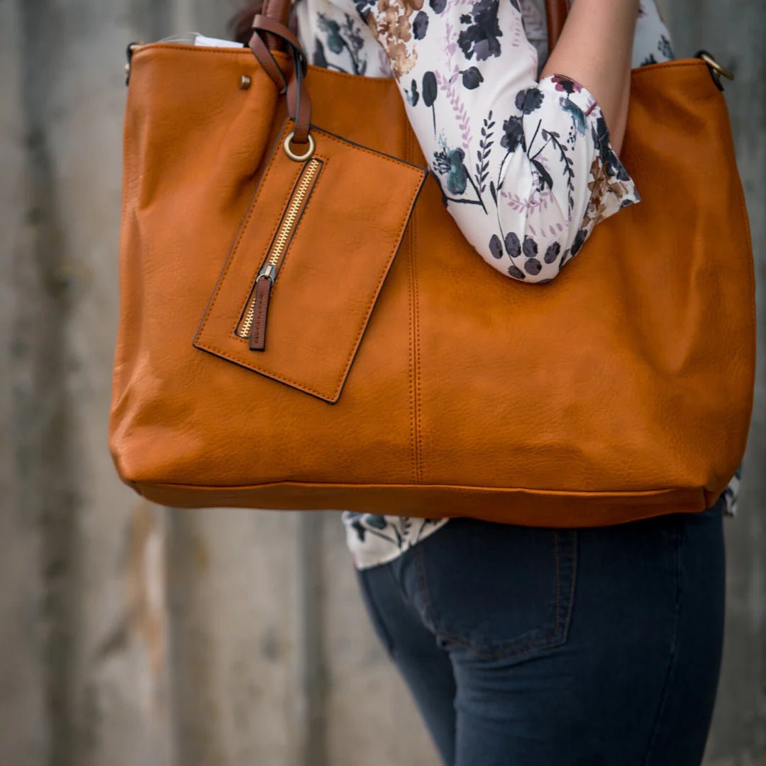 Person holding a large brown leather bag with a blurred background - okotoks hc pharmacy