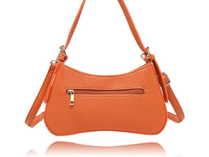 An orange pebbled faux-leather shoulder bag with a curved crescent shape, featuring a front zippered pocket with a gold-tone zipper pull and a matching adjustable shoulder strap, shown on a white background with a reflection below. - okotoks hc pharmacy