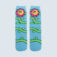 A pair of light blue crew socks featuring a cartoon floral pattern with pink flowers, yellow smiling faces, and green vines on a light gray background. - okotoks hc pharmacy