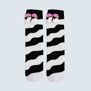 A pair of novelty socks featuring a black and white wavy zebra-like stripe pattern, with a cartoon face detail at the top showing pink eyebrows and white eyes, set against a solid light gray background. - okotoks hc pharmacy