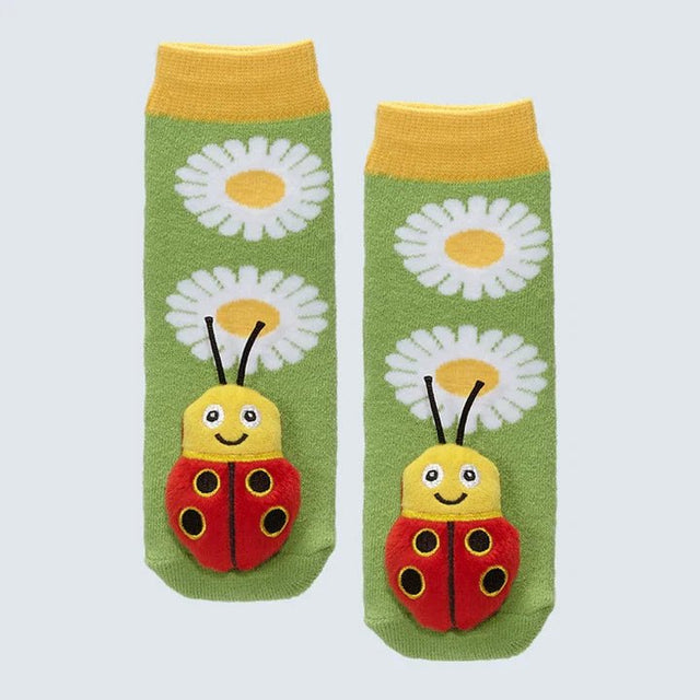 A pair of green baby socks with yellow cuffs, featuring white daisy patterns and a red ladybug applique on the front, displayed against a light gray background. - okotoks hc pharmacy