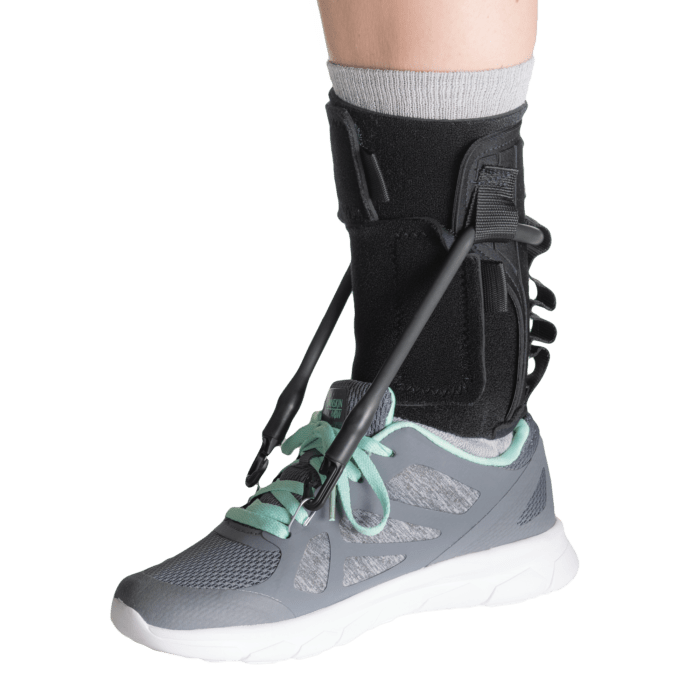 Ankle support brace on a foot wearing a gray athletic shoe with green accents. - okotoks hc pharmacy