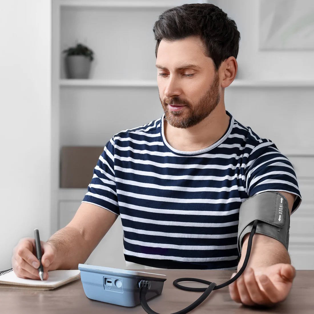 Man taking his blood pressure at home using a device, wearing a striped shirt. - okotoks hc pharmacy