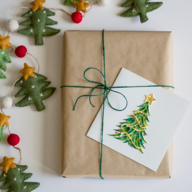 Gift wrapped in brown paper with a green ribbon, surrounded by Christmas decorations on a white background. - okotoks hc pharmacy